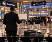 Chauffeur holding a name sign at airport baggage claim for a meet-and-greet pickup, with a black SUV waiting outside.